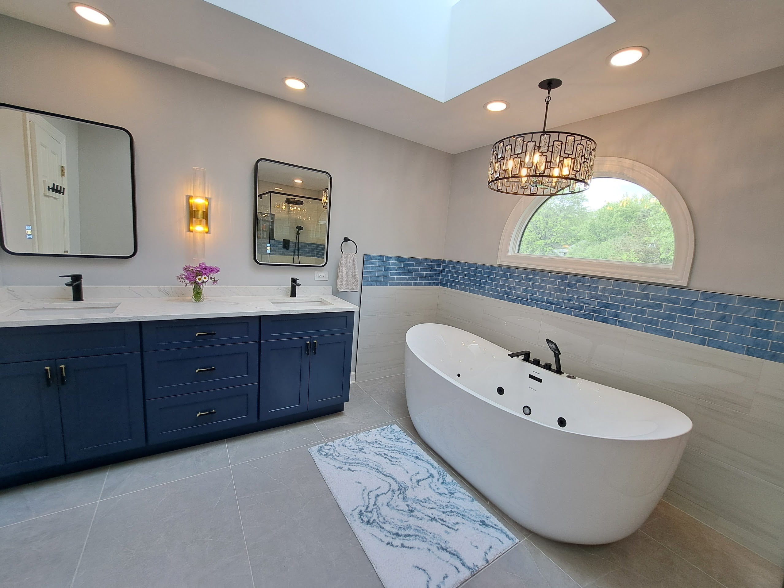 Bathroom vanity with blue cabinetry, double mirrors, and freestanding tub in a modern bathroom