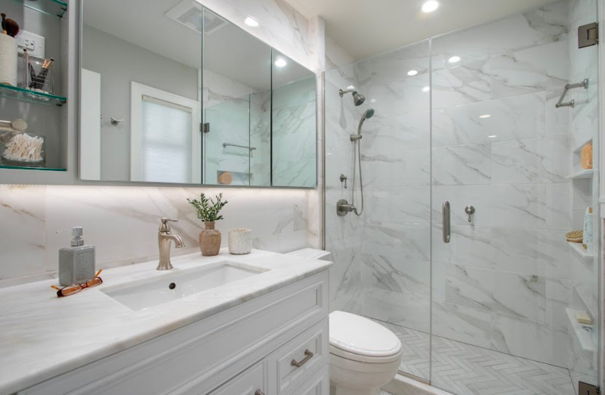 Modern white bathroom with marble tile, glass shower, and white vanity cabinets — bathroom remodeling and finish materials by Emerald Fern Finishes