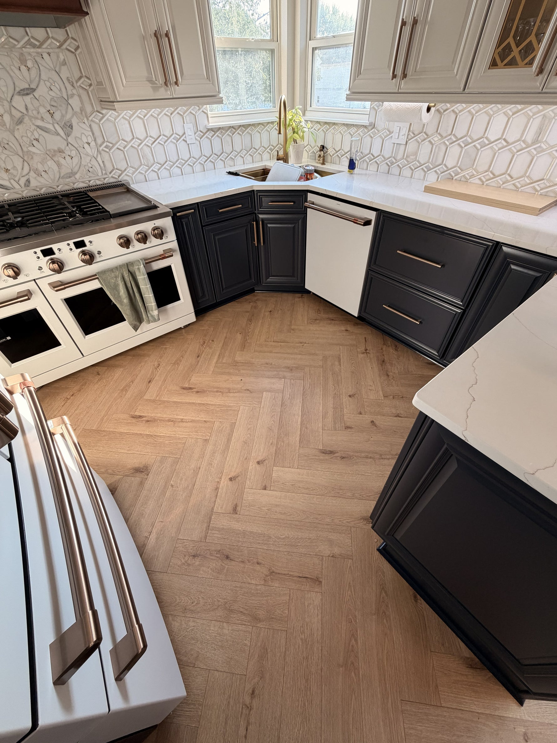 Kitchen with herringbone hardwood flooring, dark shaker cabinets, quartz countertops, and geometric tile backsplash