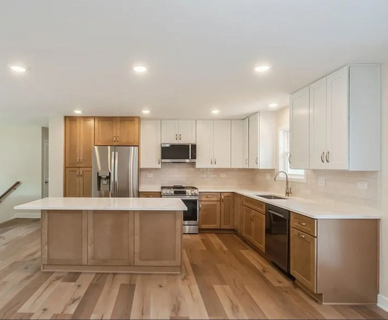 Two-tone kitchen with caramel shaker base cabinets, white upper cabinets, quartz countertops, and light hardwood floors