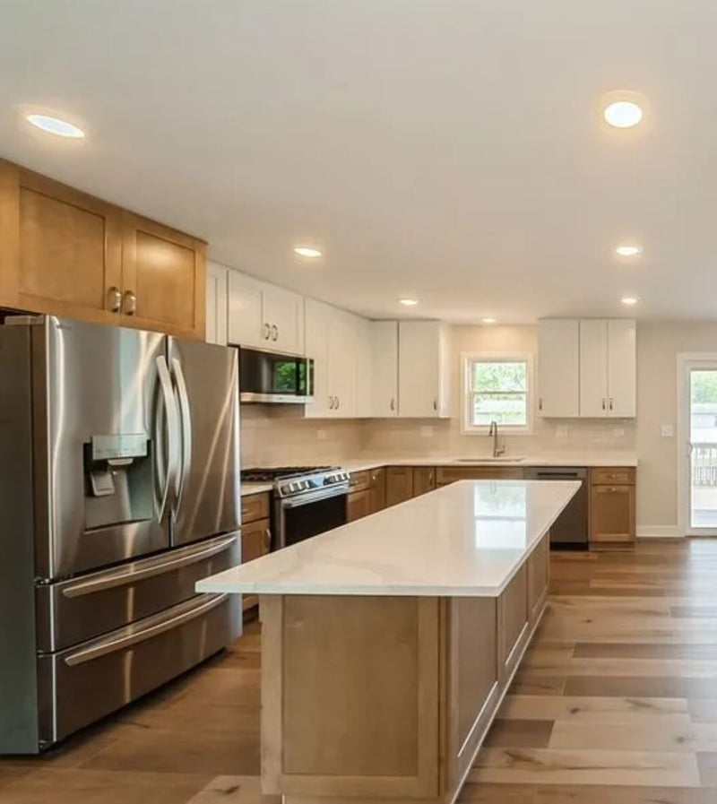 Two-tone kitchen with white upper cabinets, natural wood lower cabinets and island, white quartz countertop, stainless steel appliances, and hardwood floors