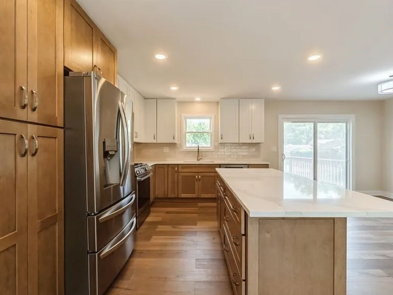 Two-tone kitchen with warm wood lower cabinets and tall pantry, white upper shaker cabinets, white quartz island countertop, subway tile backsplash, and hardwood floors