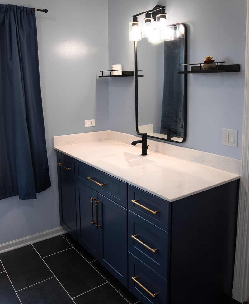 Navy blue shaker bathroom vanity with white quartz countertop, gold hardware, matte black faucet, and dark tile floor