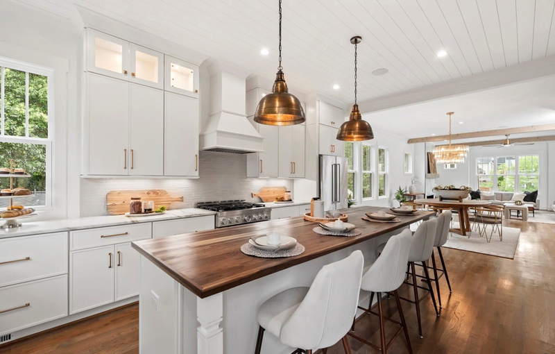 Open concept kitchen with white shaker cabinets, butcher block island, gold hardware, brass pendant lights, white range hood, and shiplap ceiling