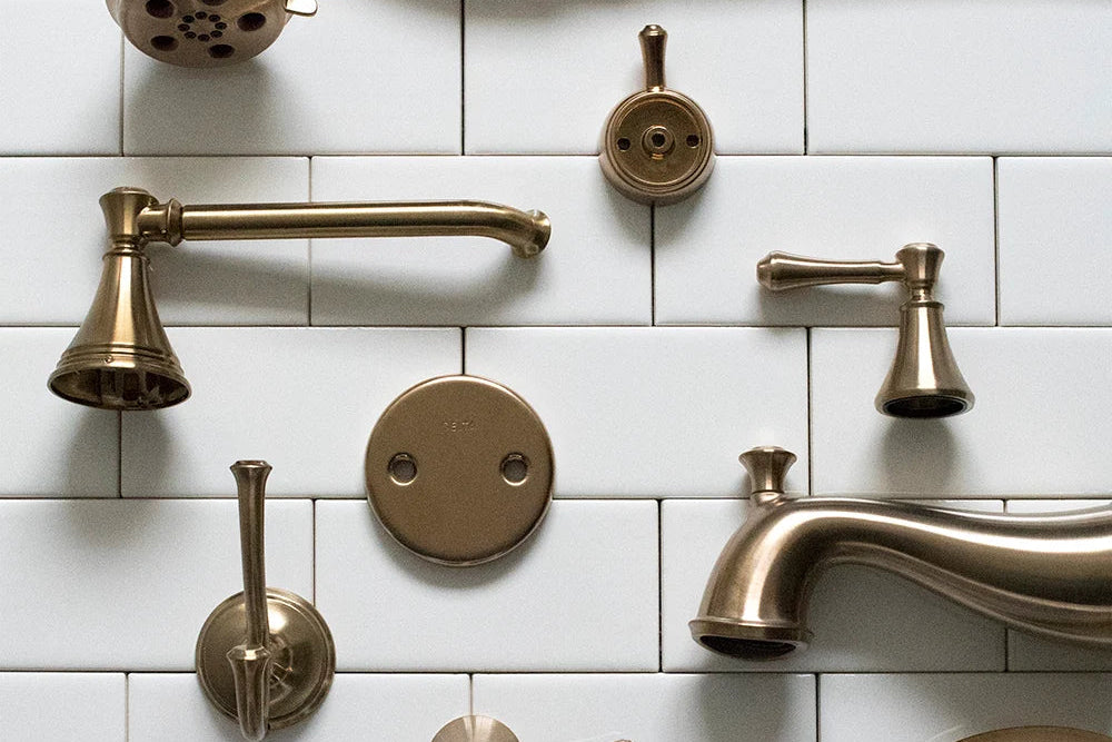 Brushed brass bathroom plumbing fixtures including faucet handles, tub spout, shower head, and valve trim on white subway tile