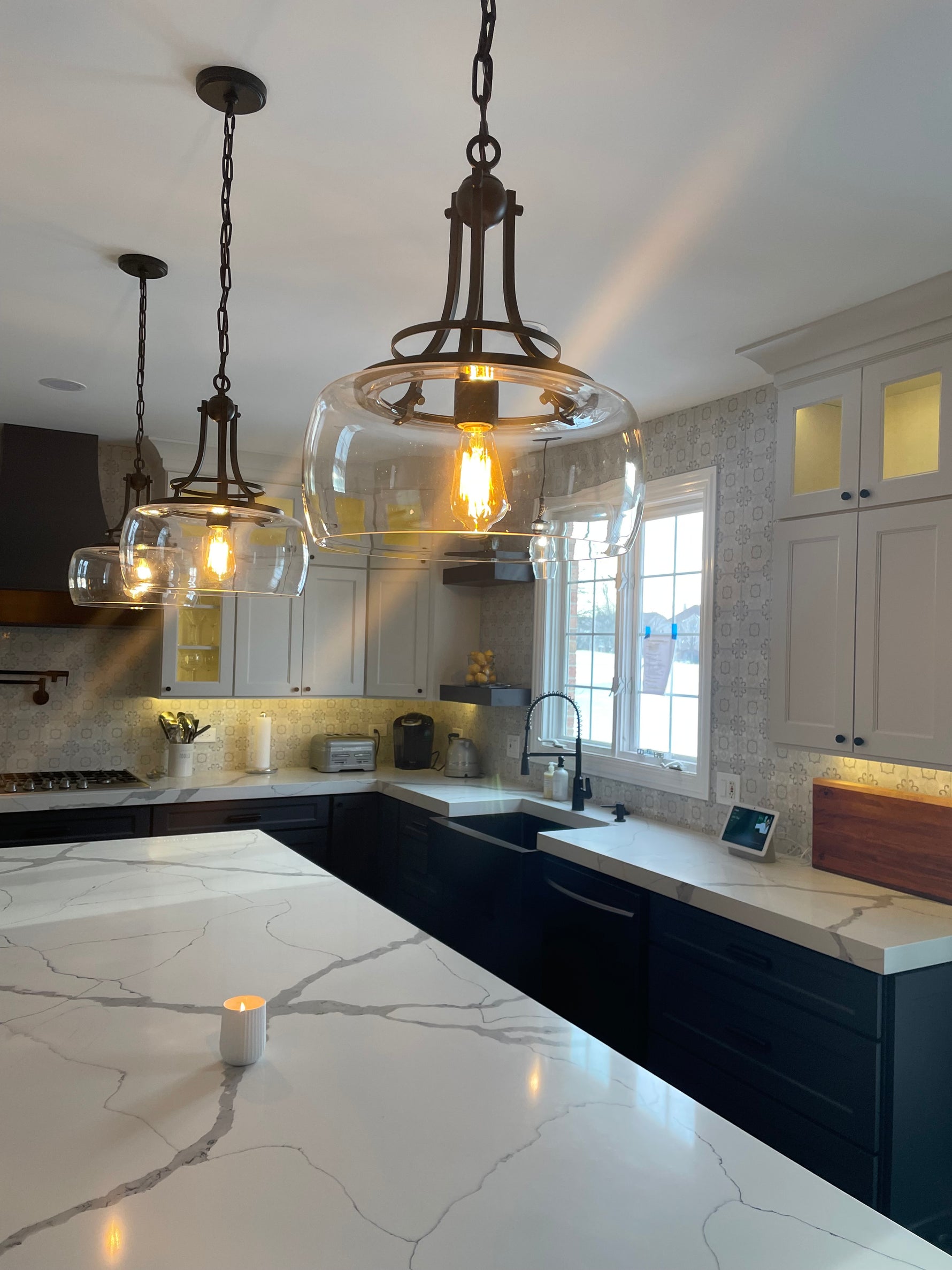 Clear glass pendant lighting over quartz countertops with modern kitchen sink and faucet, showcasing statement lighting, premium surfaces, and coordinated kitchen finishes