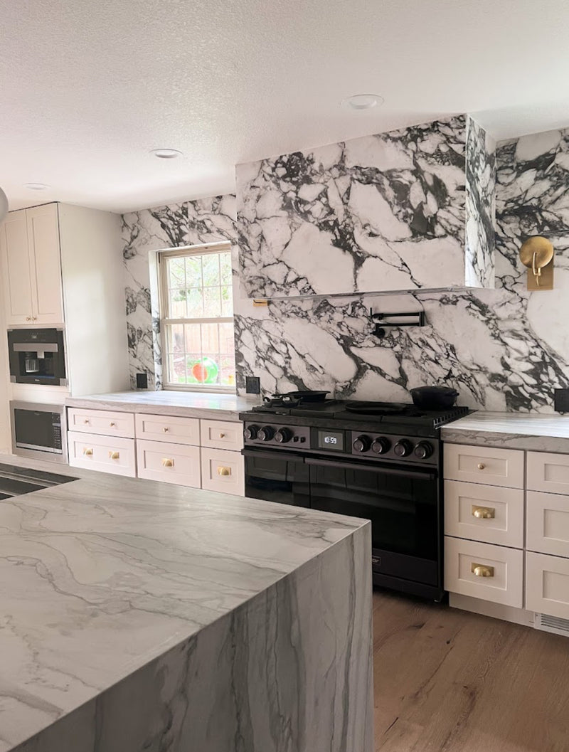 White shaker kitchen cabinets with marble slab backsplash, waterfall island countertop, and black professional range