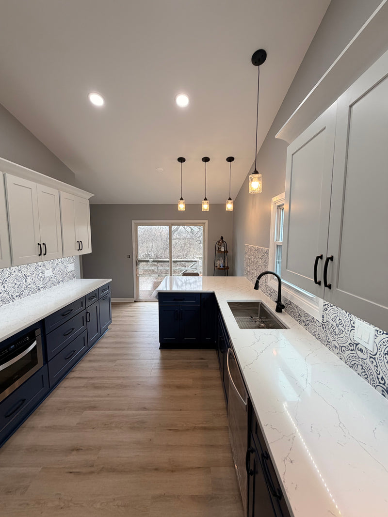 Navy and white kitchen with Rose Hill Cabinets, Paramount luxury vinyl plank flooring, MSI patterned tile backsplash, black Innovations Lighting pendants, and Top Knobs cabinet hardware, showcasing a coordinated, professional-grade kitchen finish package