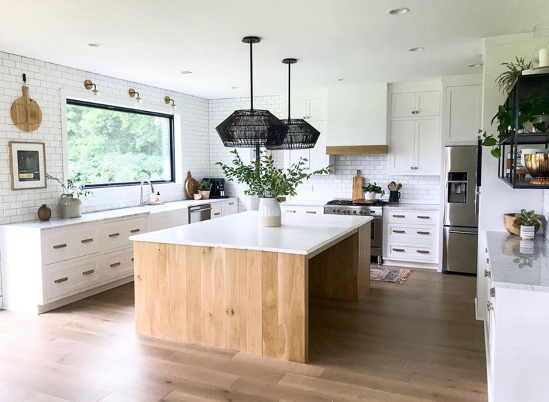 Bright kitchen with white shaker cabinets, natural wood island, white quartz countertop, subway tile backsplash, black woven pendant lights, and light hardwood floors