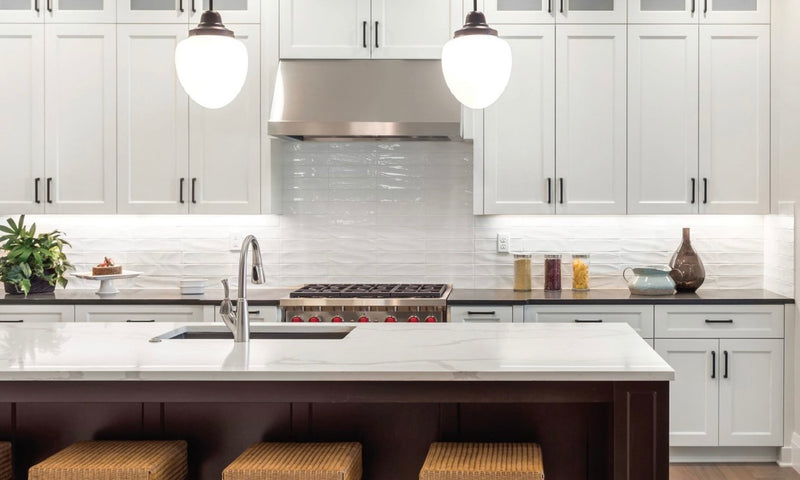 Two-tone kitchen with white shaker cabinets, dark wood island, white marble quartz countertop, textured white tile backsplash, stainless steel range hood, and globe pendant lights