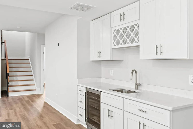 White shaker wet bar cabinets with built-in wine fridge, lattice wine rack wall cabinet, white quartz countertop, and undermount sink