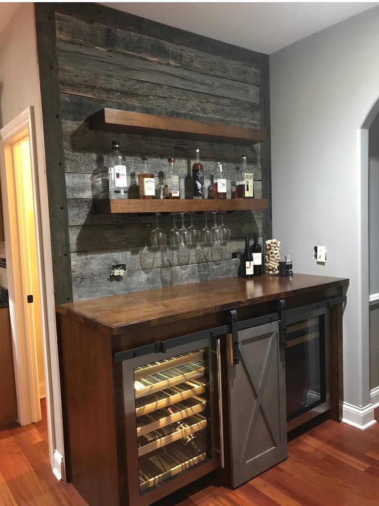 Custom dark wood home bar cabinet with barn door, wine fridge and reclaimed wood accent wall