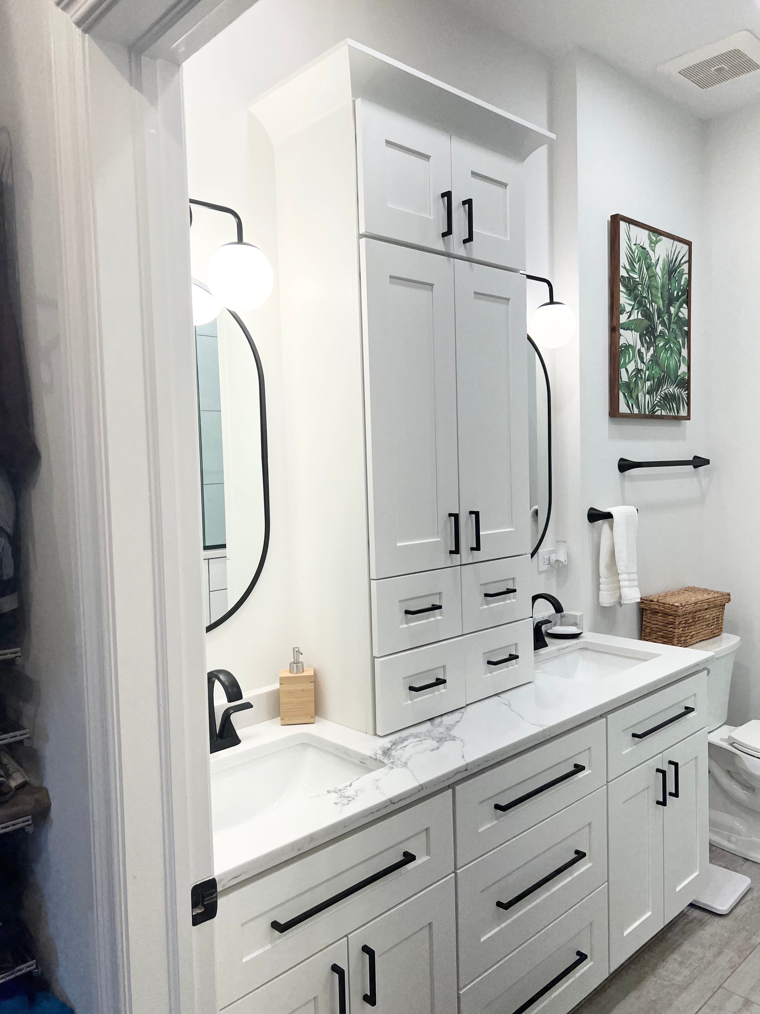 White bathroom vanity from Rose Hill Cabinets with Top Knobs hardware, paired with Daltile wall tile and Innovation Lighting sconces, showcasing coordinated cabinetry, hardware, tile, and bathroom lighting finishes