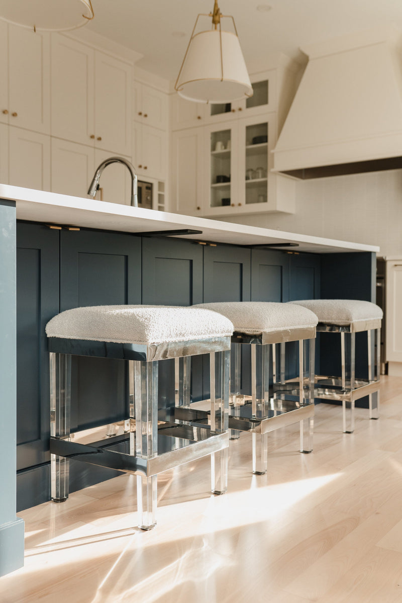 Black shaker kitchen island with white quartz countertop, lucite counter stools, white upper cabinets with glass fronts, and light hardwood floors