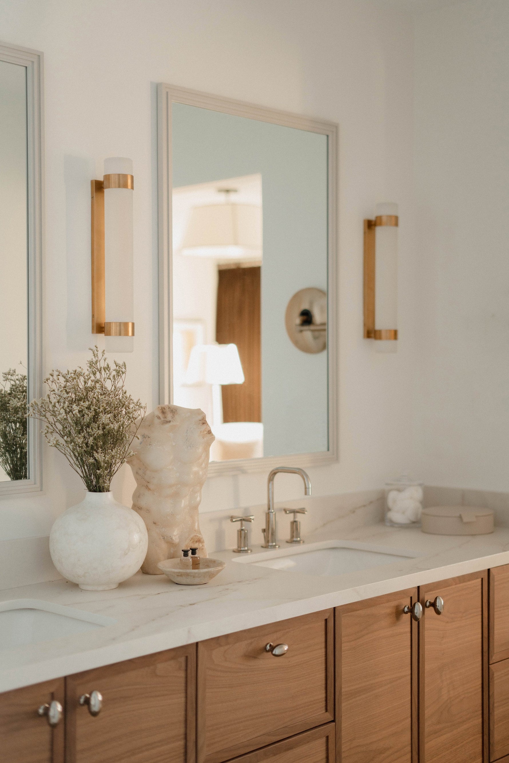 Warm wood vanity with white marble countertop, rectangular mirror, and gold sconce lighting