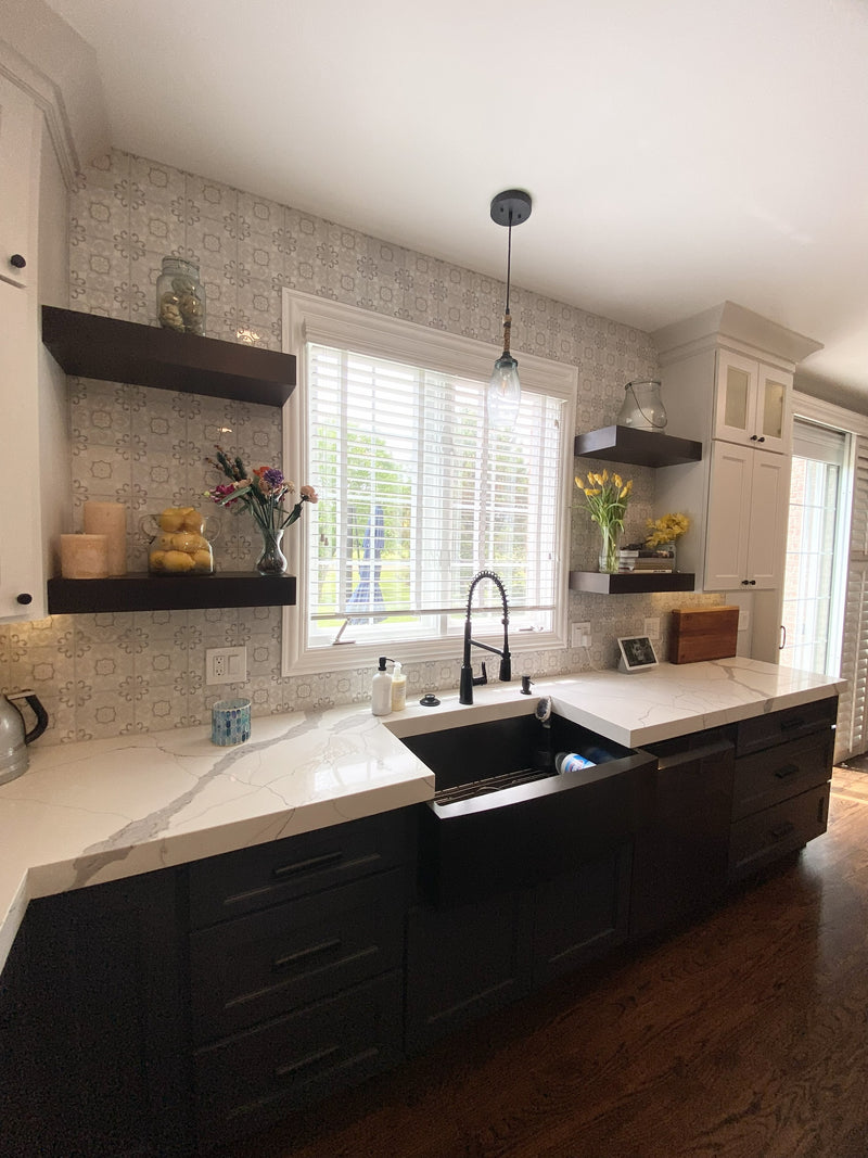 Kitchen sink area with dark charcoal base cabinets, white quartz countertop, black farmhouse sink, patterned encaustic tile backsplash, and floating dark wood shelves