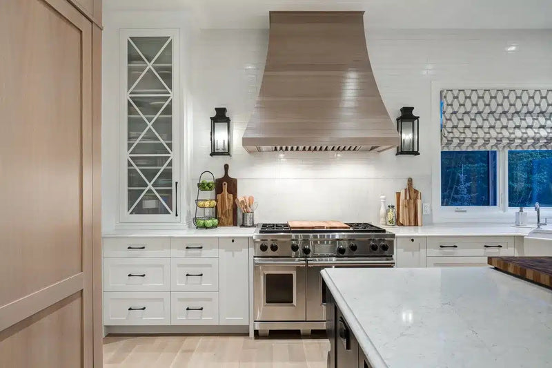 White shaker kitchen with professional gas range, stainless steel range hood, cross-mullion glass cabinet, white quartz countertop, matte black hardware, and wall sconce lighting