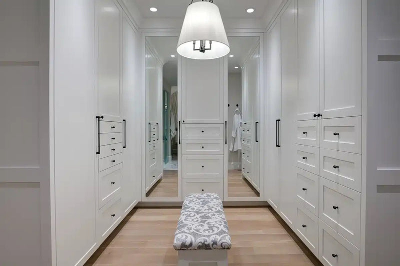 Custom walk-in closet with floor-to-ceiling white shaker cabinetry, built-in drawers, full-length mirrors, and hardwood floors