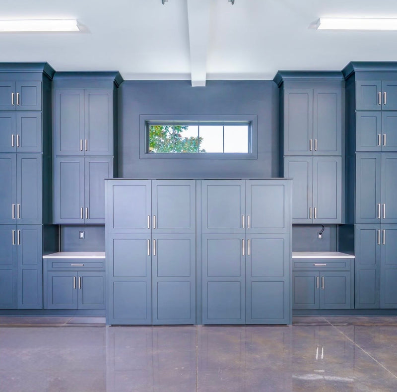 Garage with floor-to-ceiling blue shaker storage cabinets, built-in workbench countertops, tall pantry-style cabinets, and brushed nickel hardware