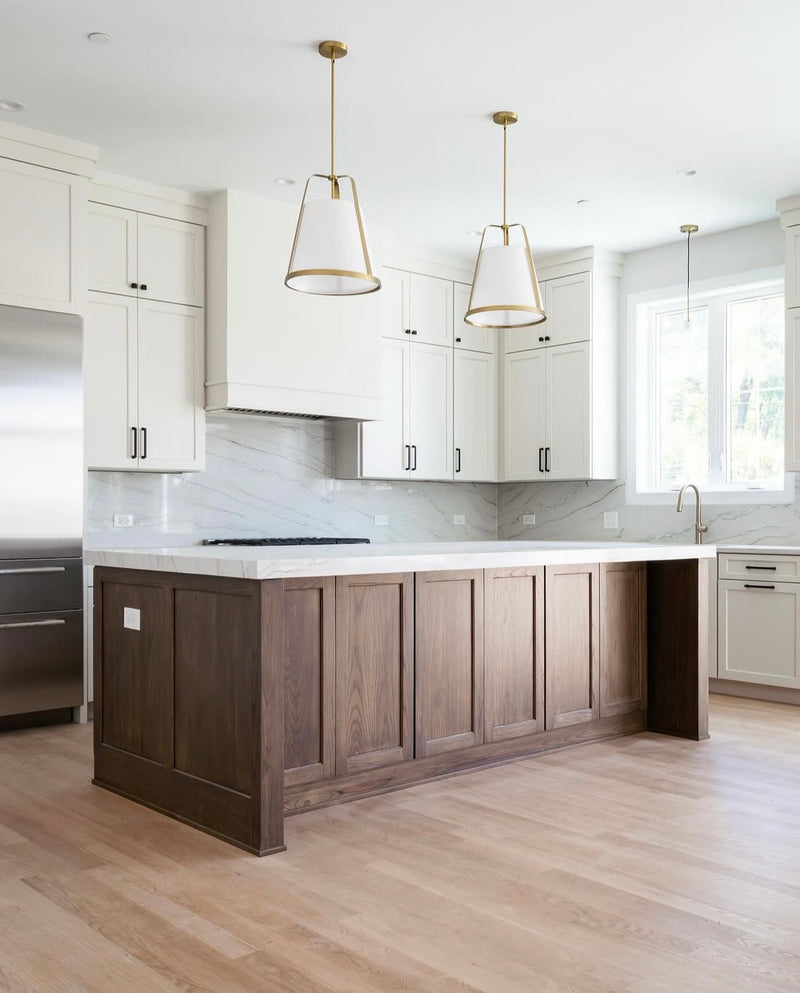 Two-tone kitchen with white shaker cabinets, stained wood panel island, marble slab backsplash, white quartz countertop, gold pendant lights, and light hardwood floors