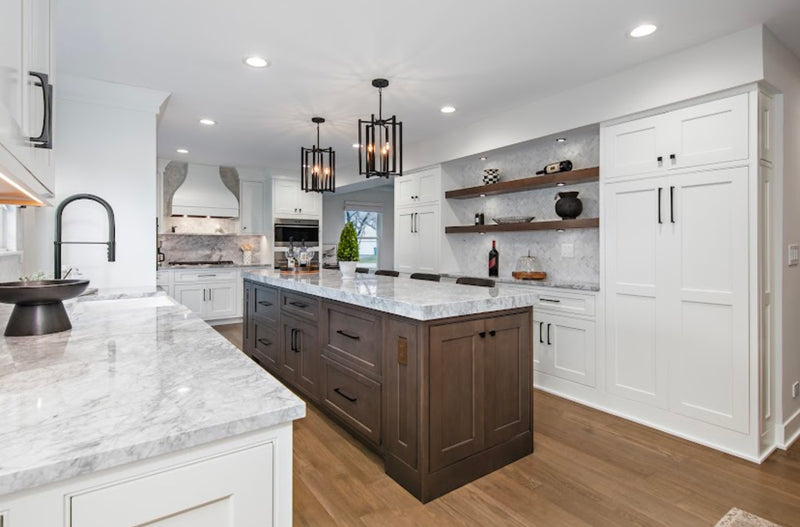 Large kitchen with white shaker cabinets, dark wood island, marble countertops, floating walnut shelves, stone backsplash, black cage pendant lights, and hardwood floors