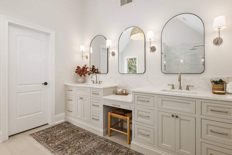 Luxury primary bathroom with gray shaker double vanity, built-in makeup station, arched mirrors, and marble countertop