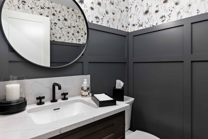 Powder room with dark charcoal board and batten walls, floral wallpaper, marble quartz vanity top, matte black faucet, dark wood vanity, and round black mirror