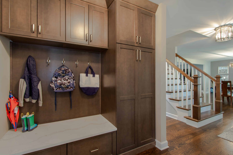 Custom mudroom with dark stained shaker cabinets, built-in coat hooks, quartz bench top, and tall pantry-style storage