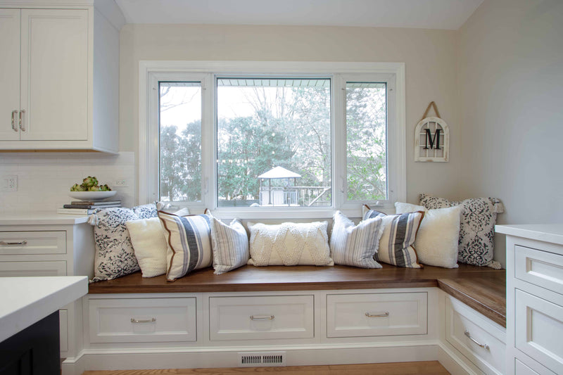 Custom built-in window seat with white shaker cabinet storage drawers, walnut wood bench top, and decorative pillows