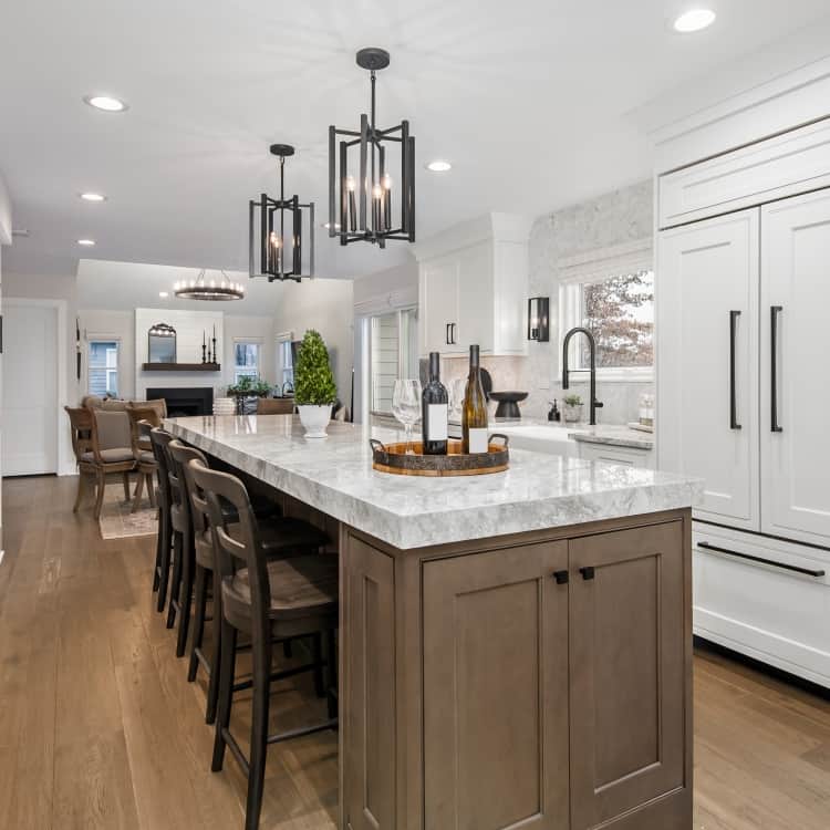 Open concept kitchen with white shaker cabinets, stained wood island, marble countertop, black hardware and pendant lights, farmhouse sink, and hardwood floors