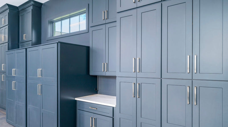 Floor-to-ceiling blue shaker cabinetry with brushed nickel hardware, tall pantry cabinets, and built-in desk with marble countertop