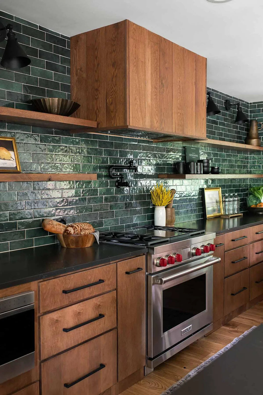 Medium wood kitchen cabinets with dark green glazed subway tile backsplash and black countertops