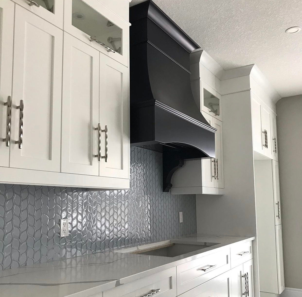 White shaker kitchen with Rose Hill cabinets, black custom range hood, textured tile backsplash, and polished quartz countertops.