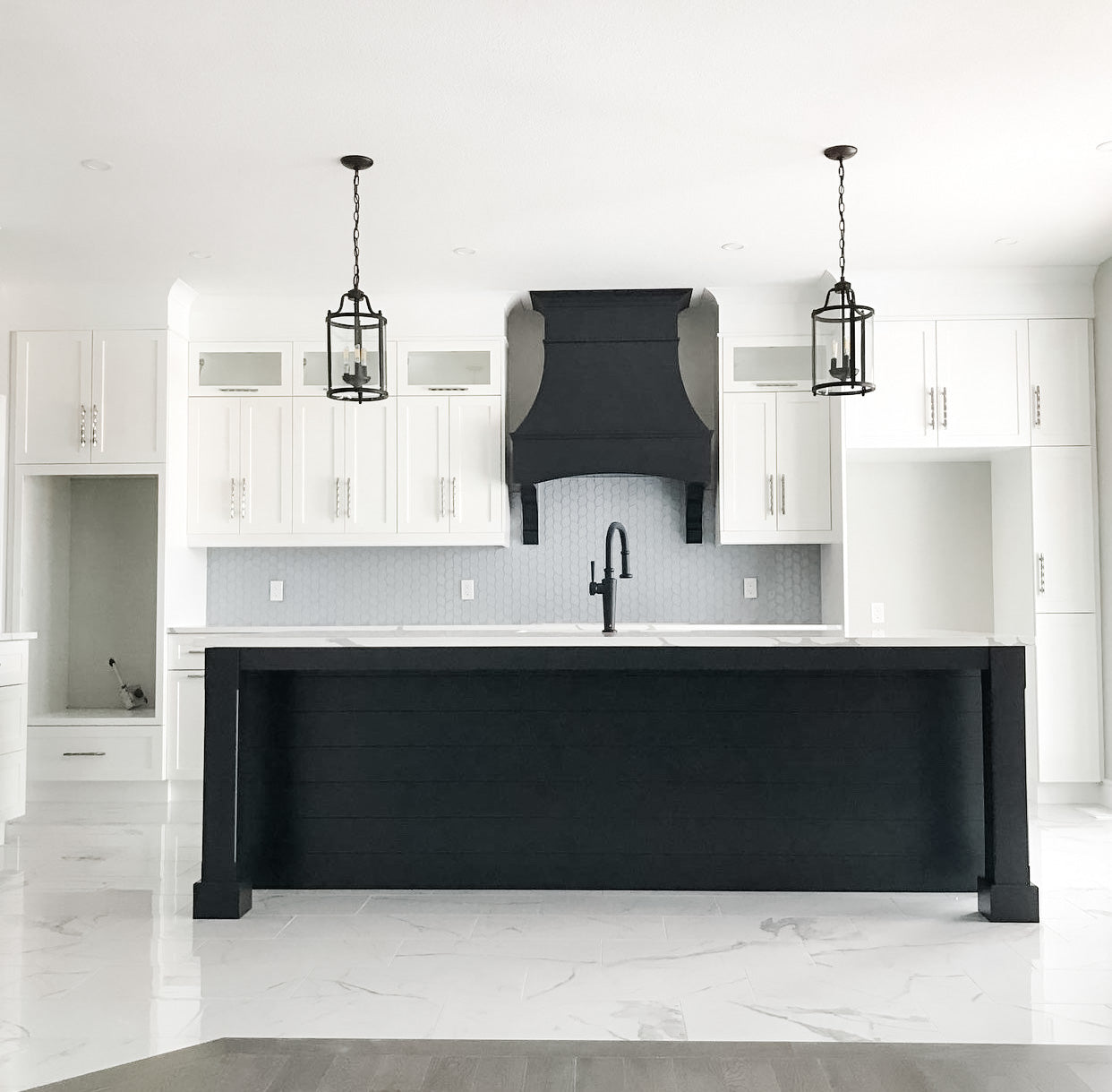Open-concept kitchen with white shaker cabinets, custom black island, quartz countertops, and Decovita porcelain floor tile showcasing a balanced mix of stock cabinetry and custom craftsmanship