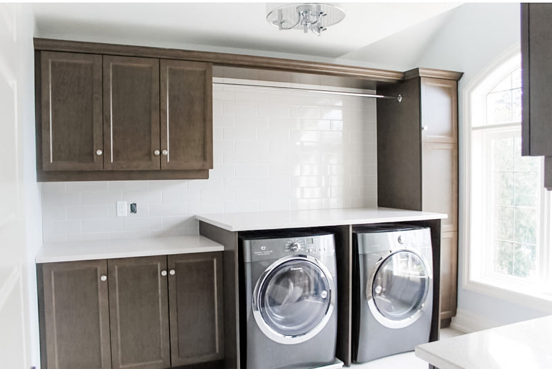 Laundry room with dark stained shaker cabinets, white quartz countertop over front-load washer and dryer, built-in hanging rod, and white subway tile backsplash