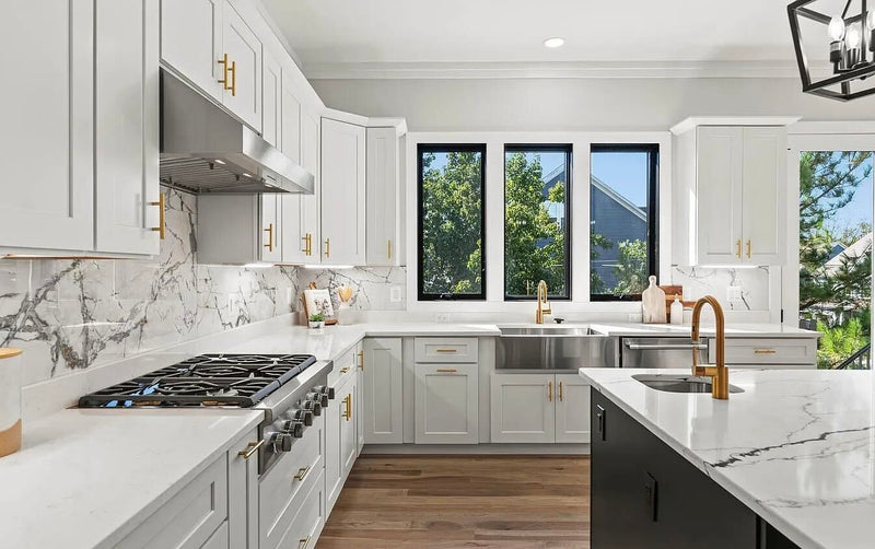 White and black shaker kitchen cabinets with brass hardware, marble slab backsplash, farmhouse sink, white quartz countertops, and black window frames