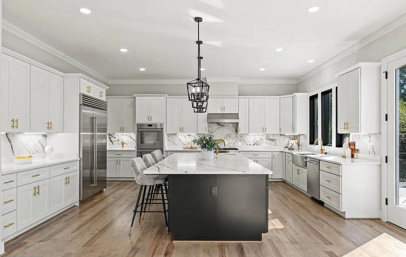 Large open kitchen with white shaker cabinets, black island, marble quartz countertops and backsplash, brass hardware, and hardwood floors