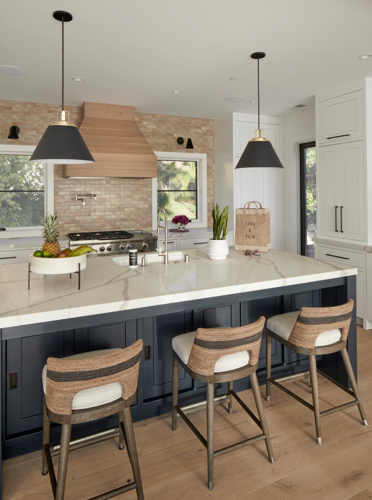 Modern kitchen island featuring pendant lighting, quartz countertops, wood range hood, and integrated sink fixtures, highlighting layered lighting and high-end kitchen finishes