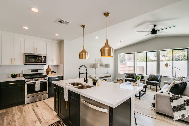 11:29 AM
Open concept kitchen with white upper cabinets, dark charcoal lower cabinets, white quartz island, gold hardware and pendant lights, subway tile backsplash, and light hardwood floors