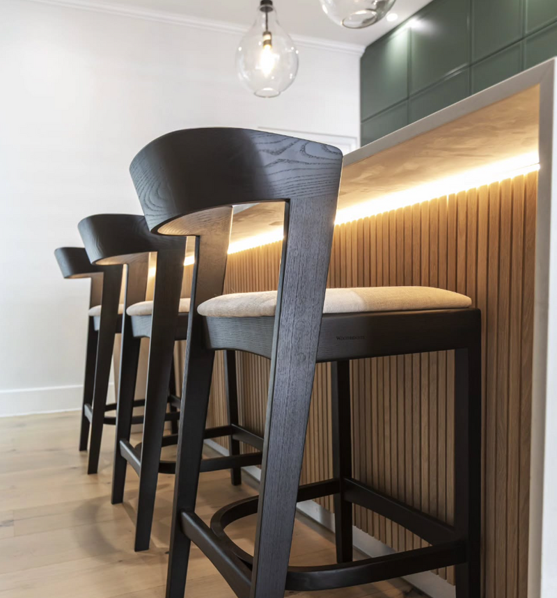 Kitchen island detail with fluted wood panel, LED underlighting, deep green upper cabinets, and black upholstered bar stools