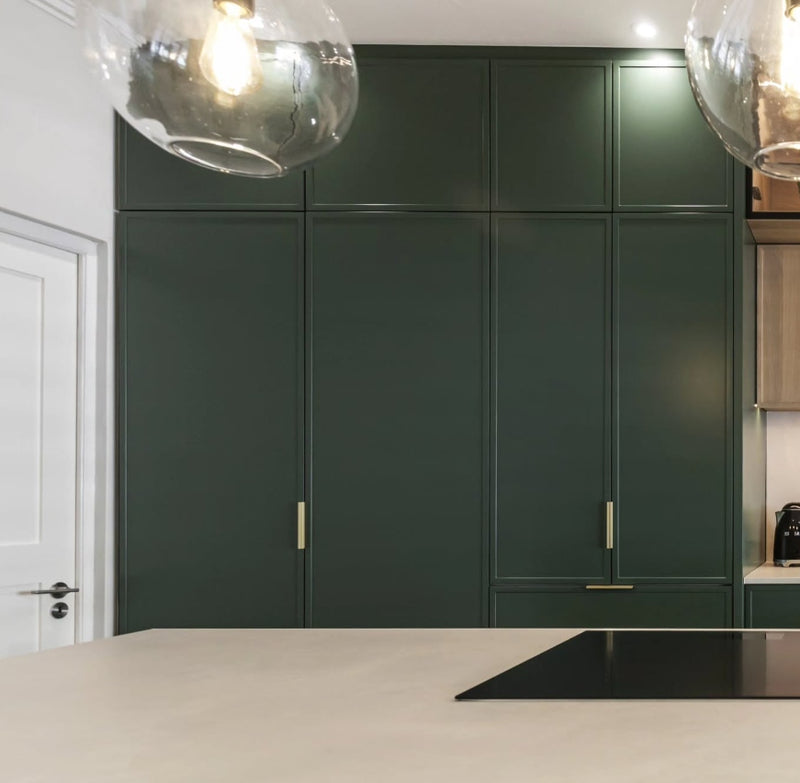 Floor-to-ceiling deep green shaker pantry and tall cabinets with slim gold hardware and cream countertop