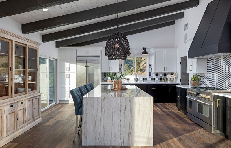 Rustic modern kitchen with white upper shaker cabinets, black lower cabinets, dramatic marble waterfall island, geometric tile backsplash, dark exposed beam ceiling, and woven pendant light