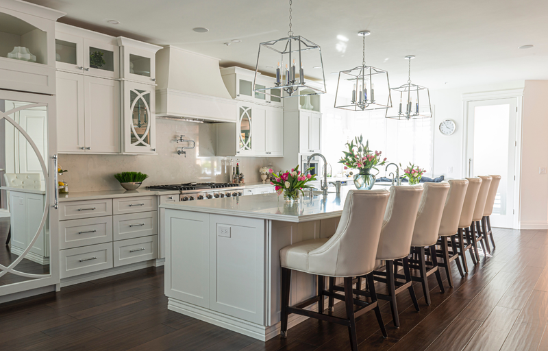 Grand white kitchen with floor-to-ceiling cabinetry, decorative mullion glass uppers, large center island, marble countertops, chrome lantern pendants, professional range, and dark hardwood floors