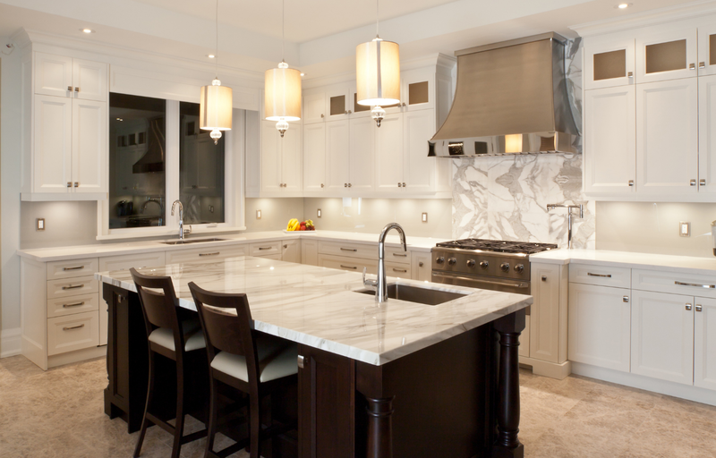 Grand kitchen with white shaker cabinets, dark wood island with marble countertop and prep sink, marble slab backsplash, stainless steel range hood, and drum pendant lights