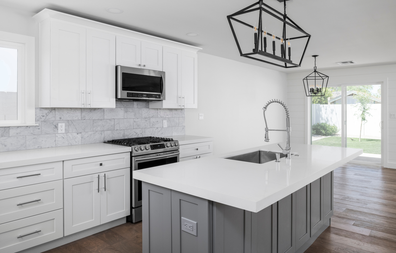White shaker cabinets with gray kitchen island, white quartz countertops, marble tile backsplash, and black cage pendant lighting