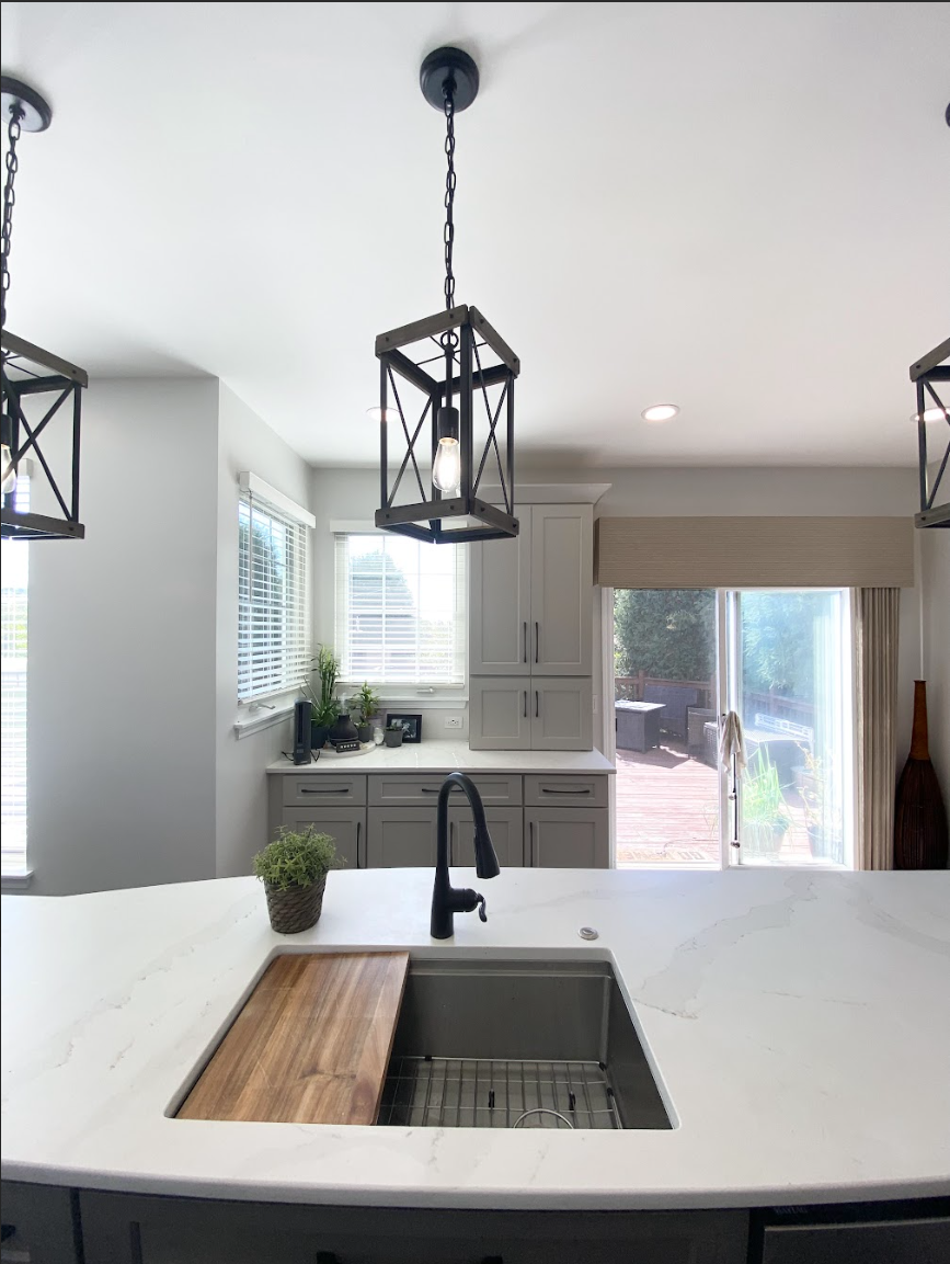 Kitchen island with undermount sink, matte black faucet, butcher block cutting board insert and white quartz countertop under black farmhouse pendant lights