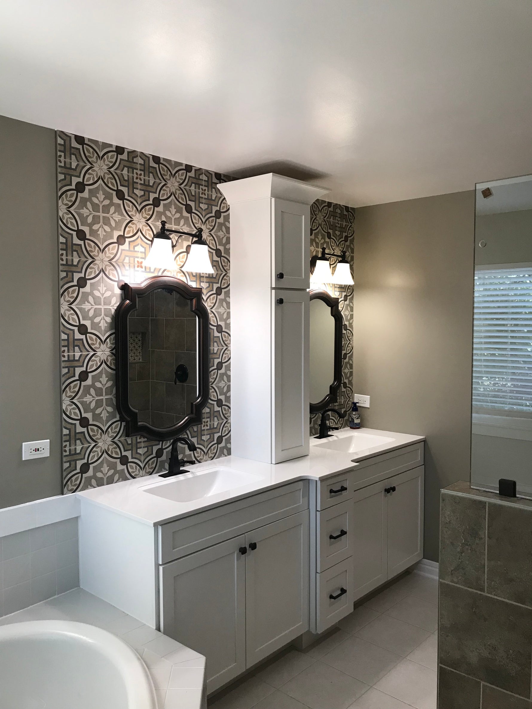 Gray shaker double vanity with ornate black mirrors, patterned tile accent wall, and wall sconces