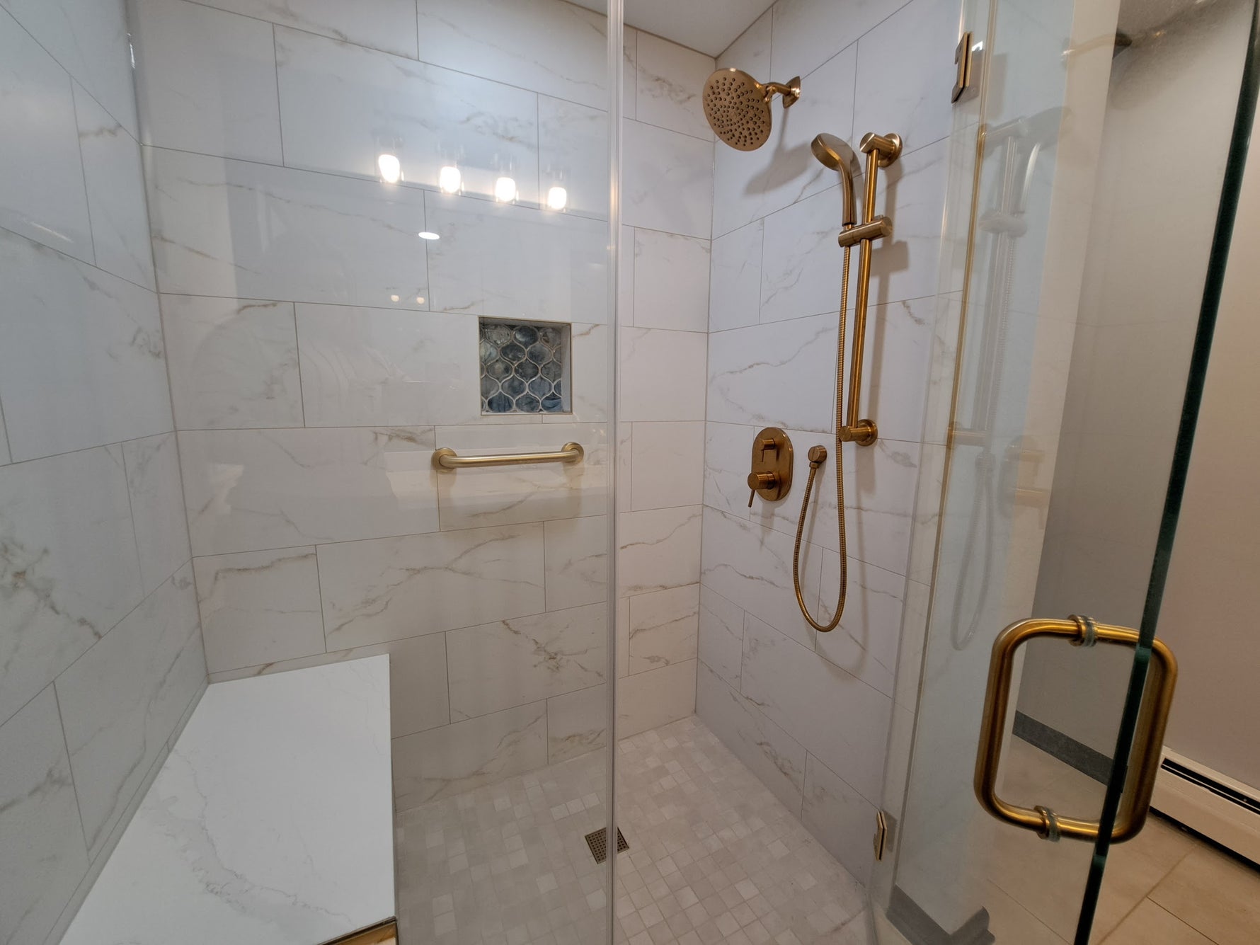 Walk-in glass shower with marble tile walls, gold fixtures, built-in niche, and mosaic floor
