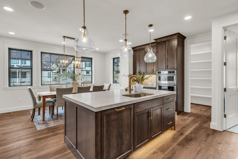 Open concept kitchen with dark stained shaker island and tall cabinets, white quartz countertop, undermount sink, gold hardware and faucet, glass teardrop pendant lights, and hardwood floors