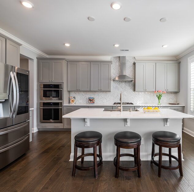Modern kitchen with stainless steel appliances, white island, gray shaker rose hill cabinets and wooden flooring.